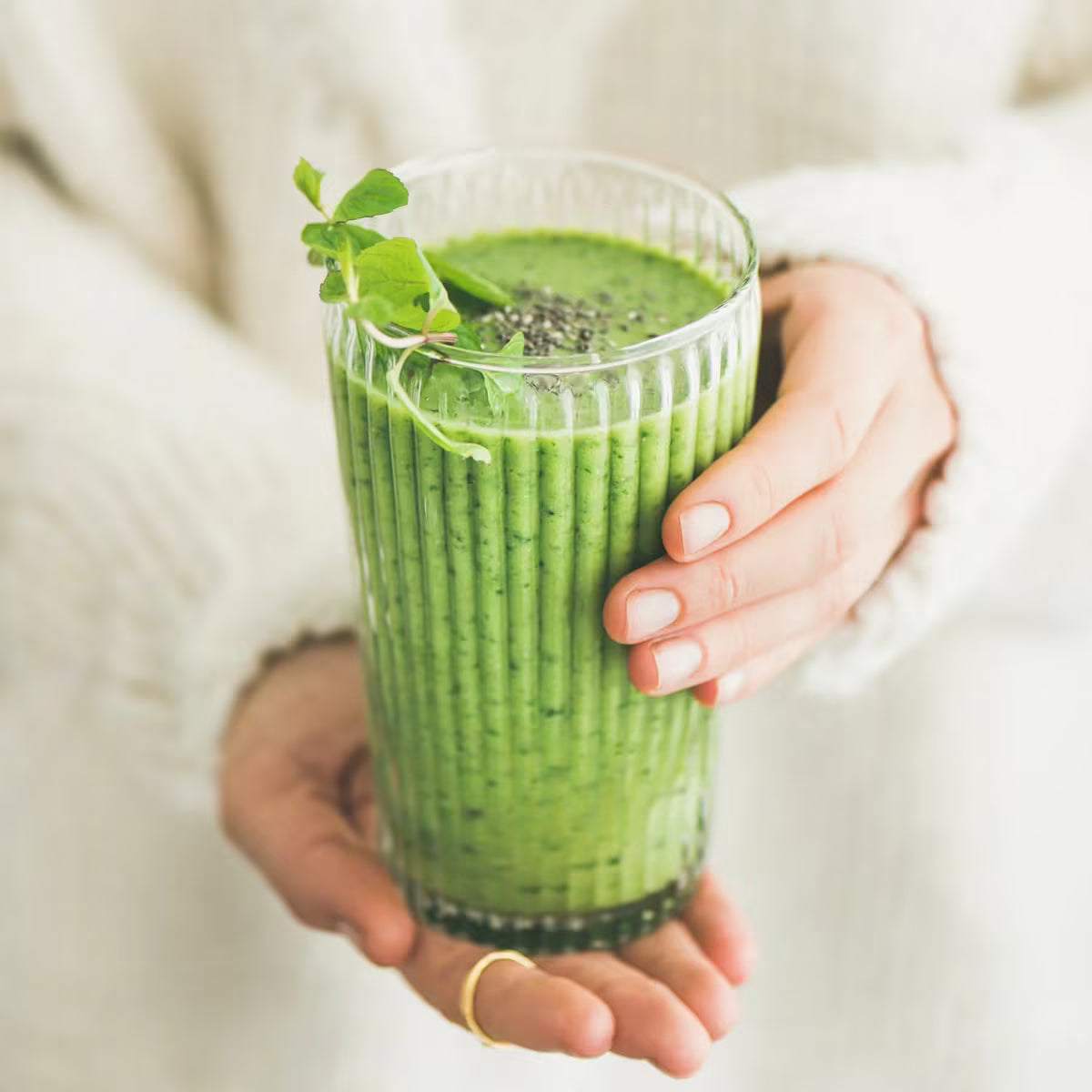 Szklanka z zielonym smoothie na bazie matchy kulinarnej trzymana w dłoniach.